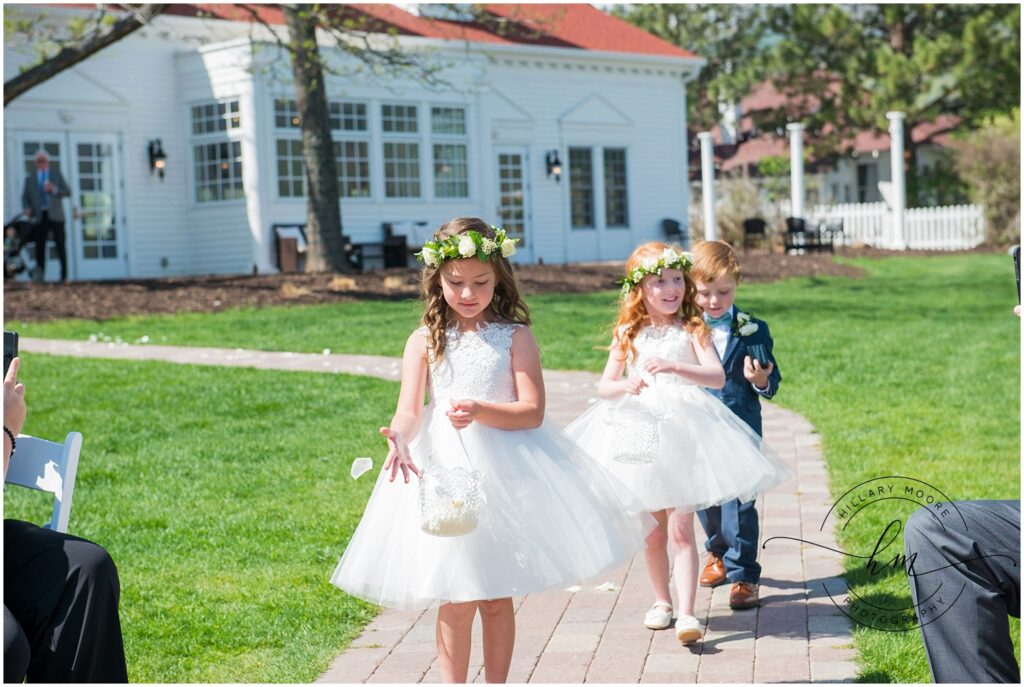 Two flower girls followed by the ring bearer walking down the stone path aisle outside.