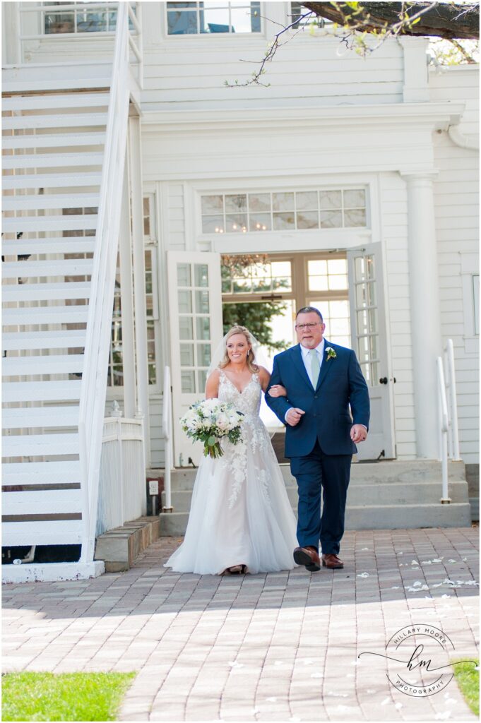 The brides father walking the bride down the stone path aisle outside.