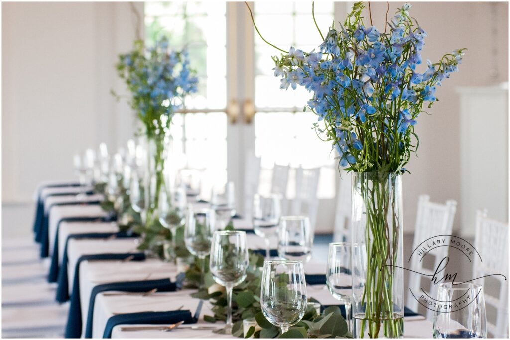 Pre-set table with wine glasses and two tall blue flower centerpieces.