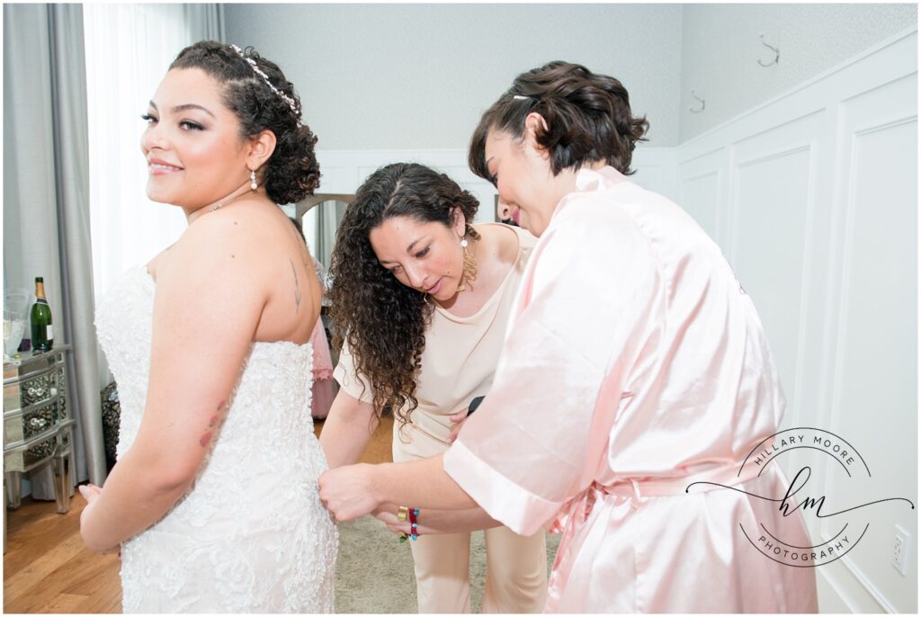 Maid of honor and mom helping bride with dress final touches.