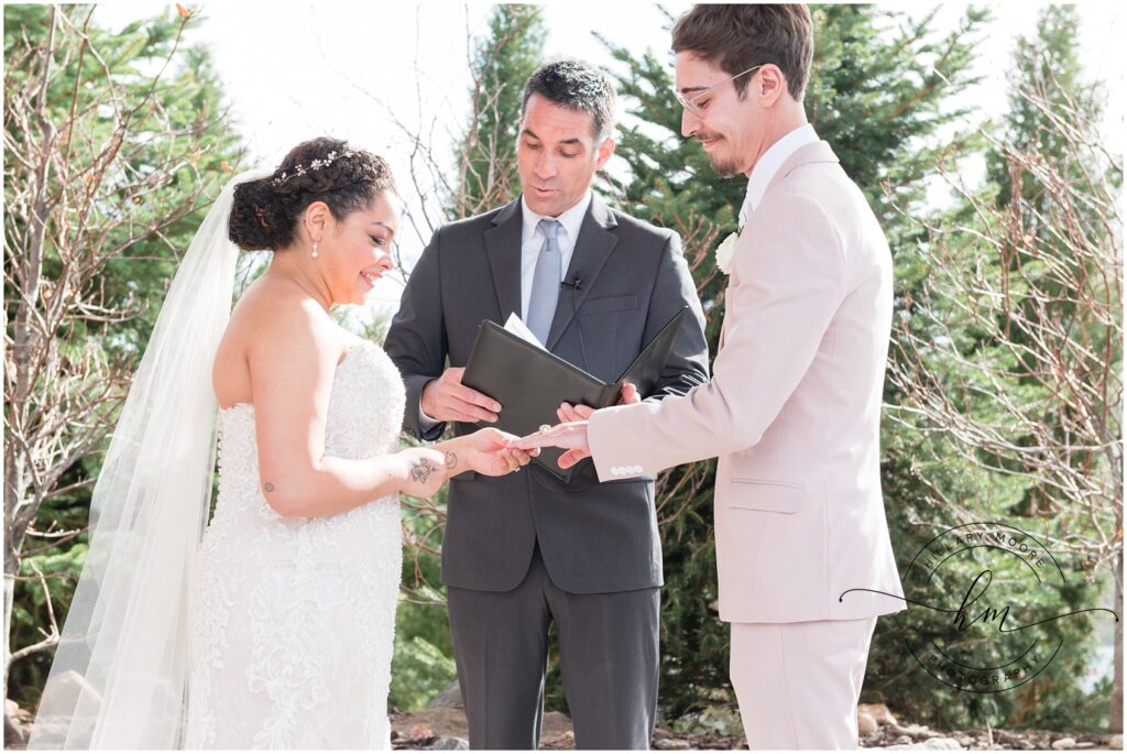 Bride putting the ring on grooms finger.