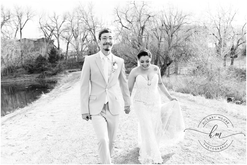 Bride and groom holding hands while walking by a pond. Black and white.