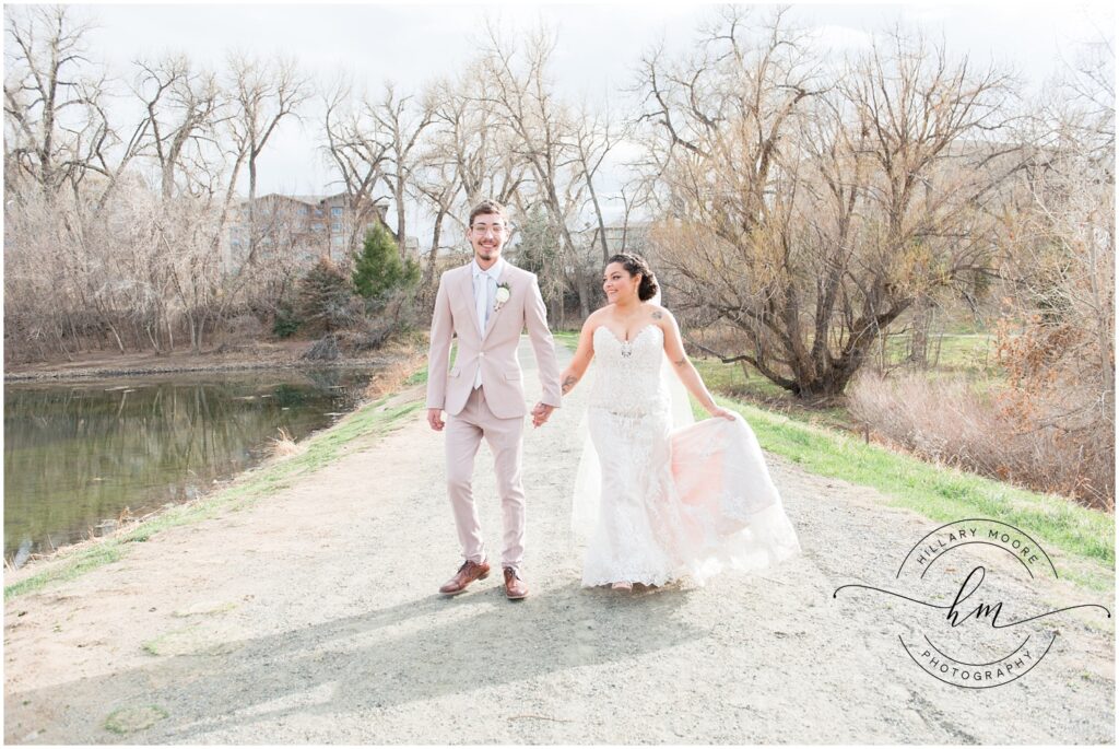 Bride and groom holding hands by a pond.