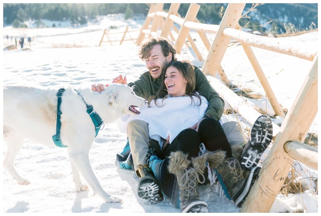 couple petting dog in snowy field by fence