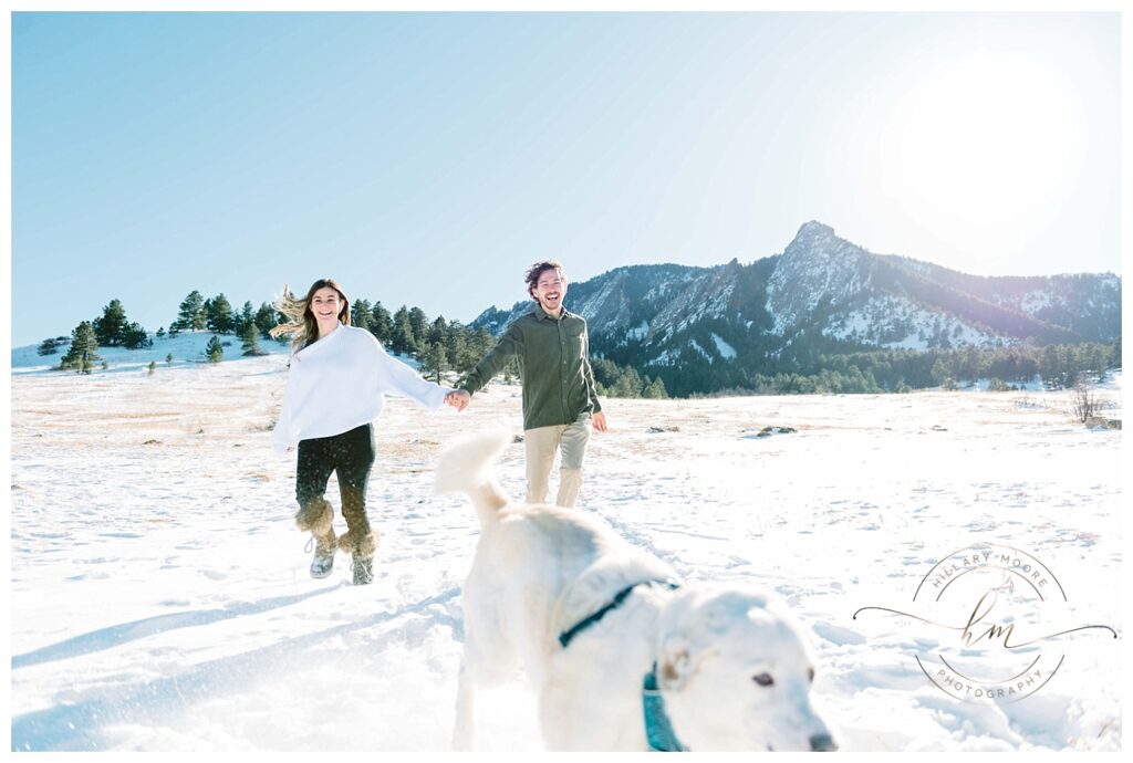 couple holding hands in snowy field with dog