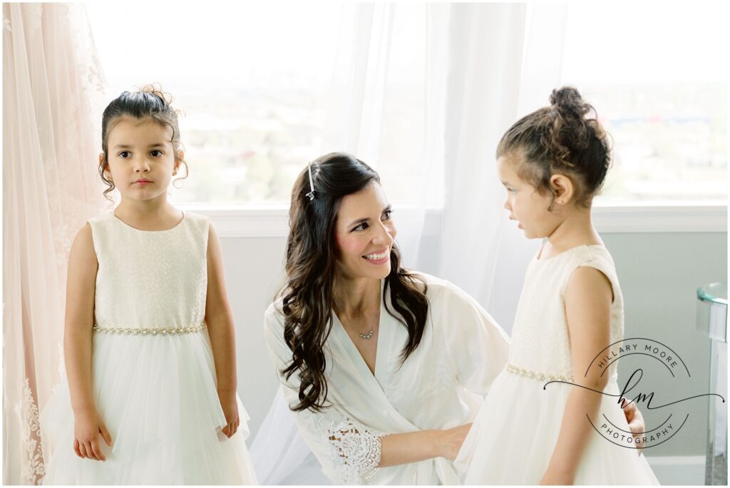 Bride is knelt down in between two flower girls before the wedding.