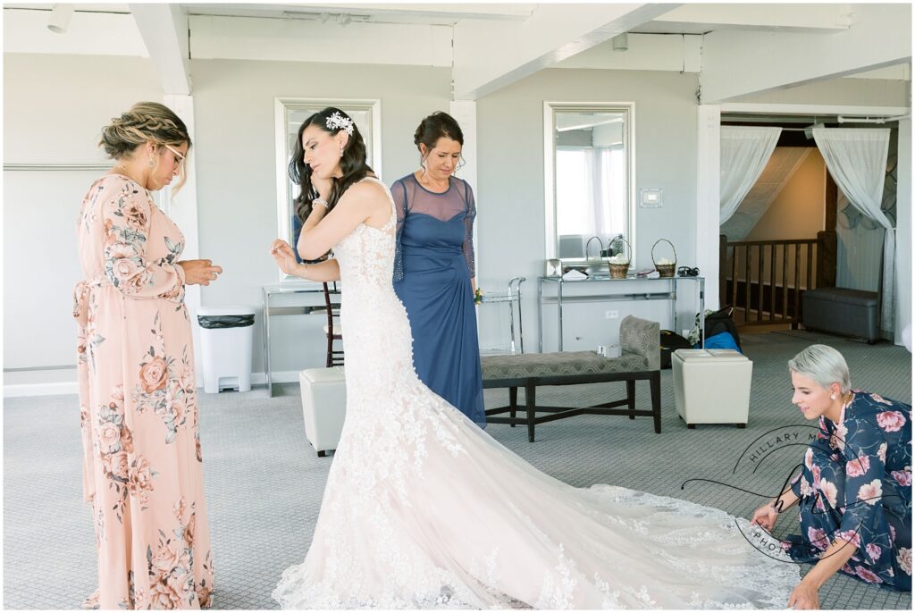 The bride with 3 women helping her get ready. One is helping her put earings in.